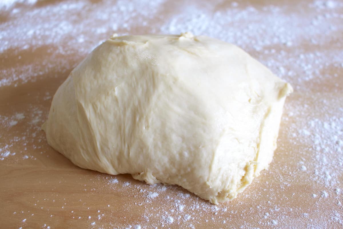 A ball of lemon cinnamon roll dough on a floured surface.