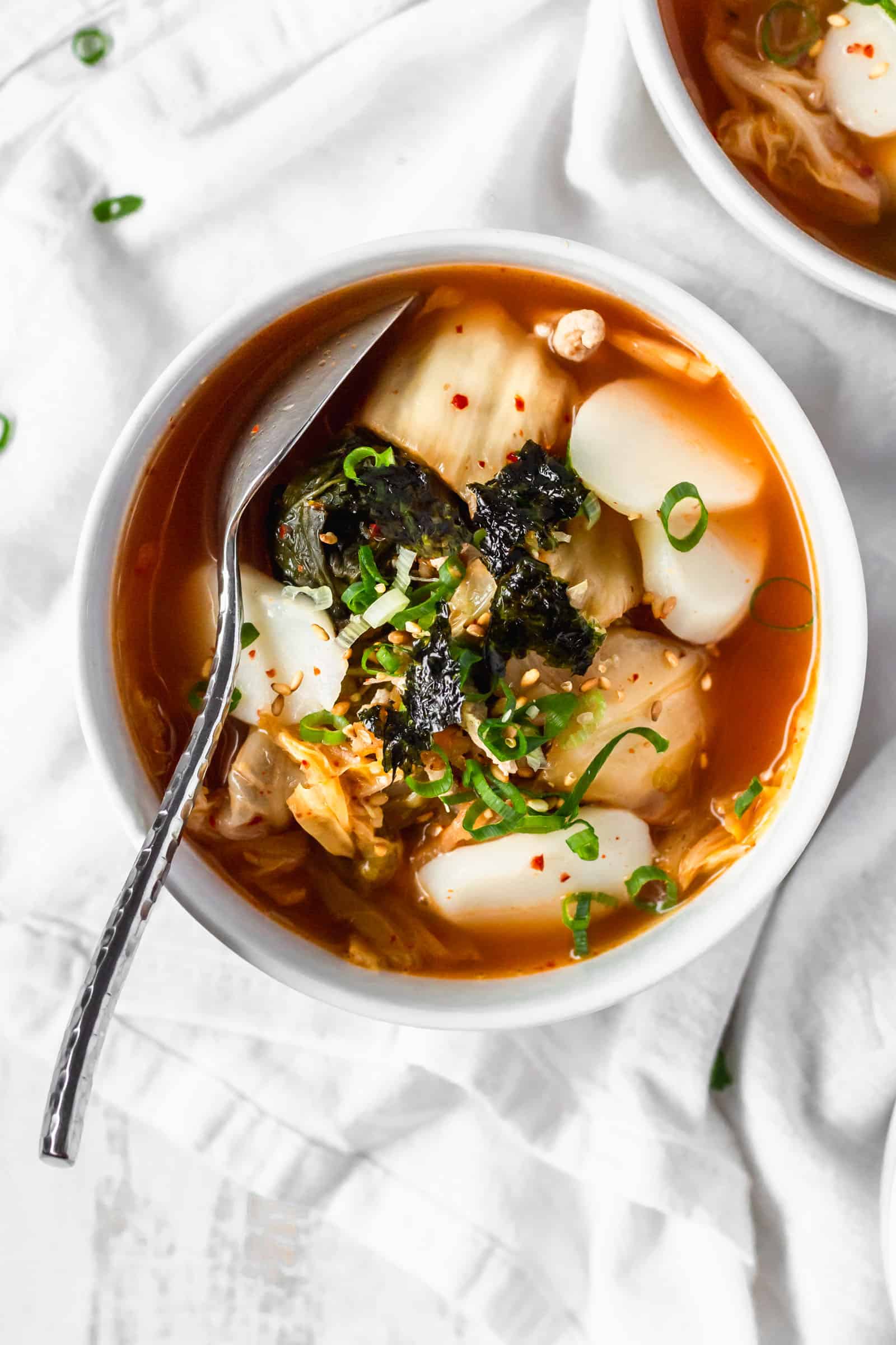 An overhead shot of a bowl of Korean rice cake soup on a white surface.