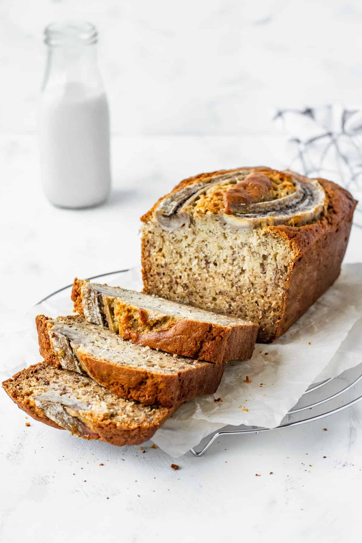 A loaf of homemade banana bread on parchment paper with three slices laid in front.