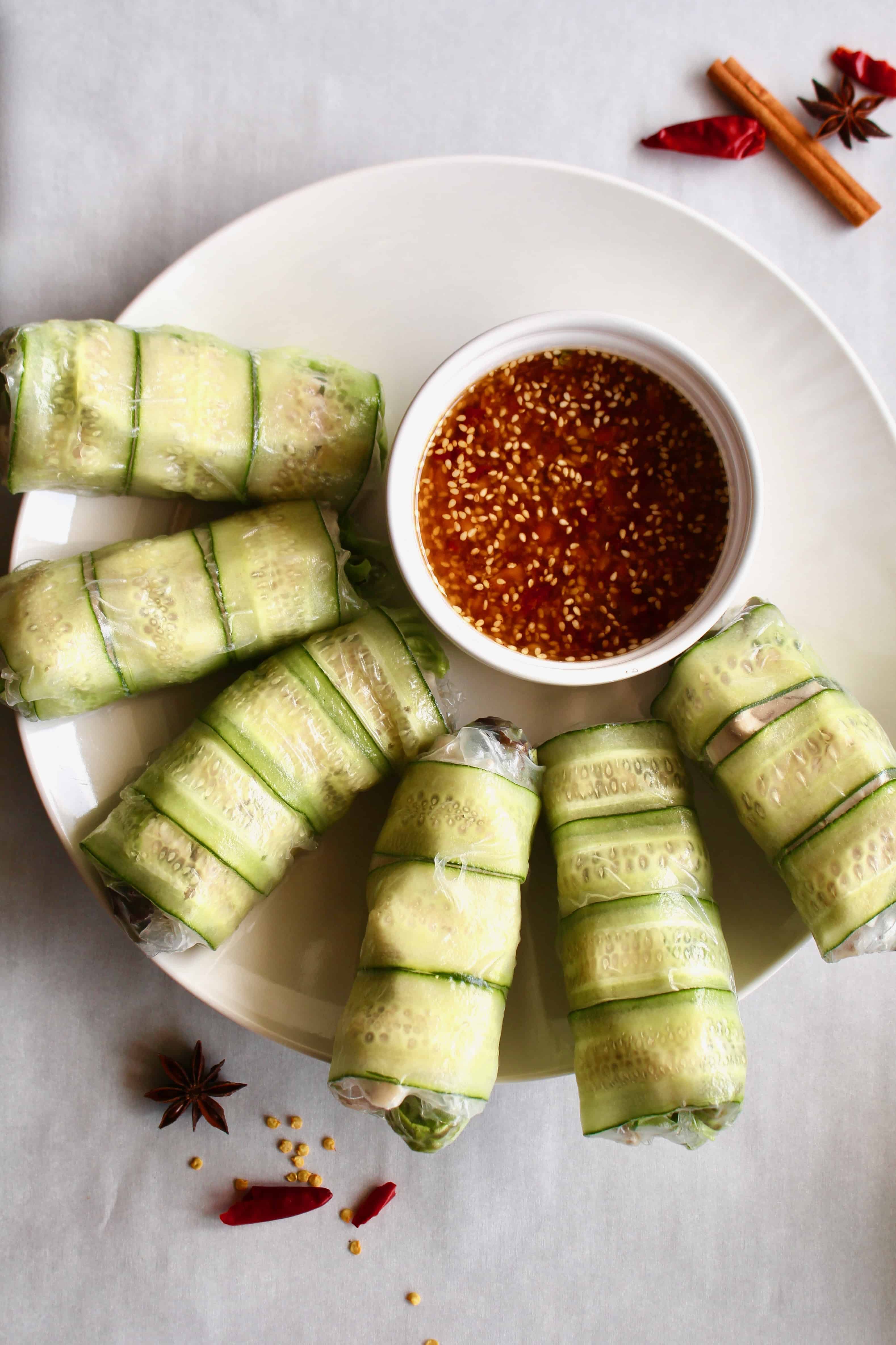 Chicken rice paper rolls on a white plate with a small bowl of spicy sauce.