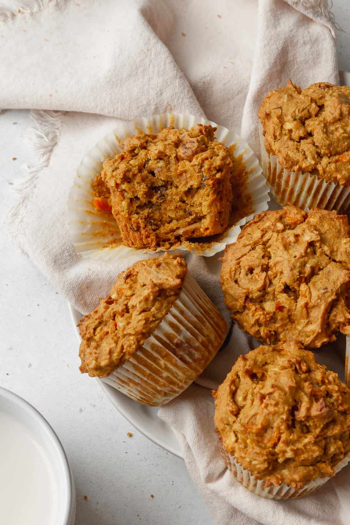 Overhead shot of morning glory muffins with one that has a bite taken out and turned on its side so you can see the moist interior.