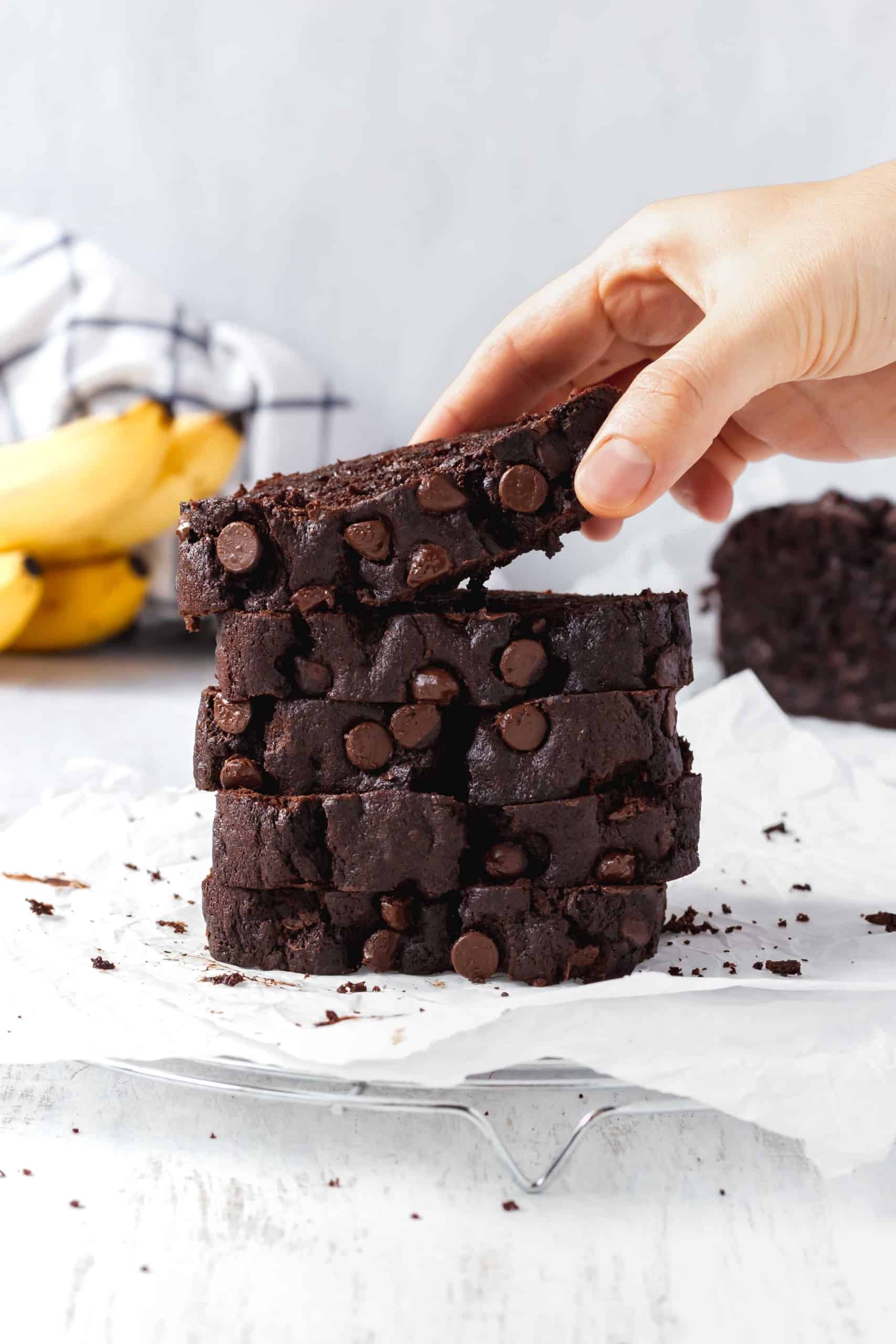 A stack of chocolate banana bread with a hand picking up a slice.