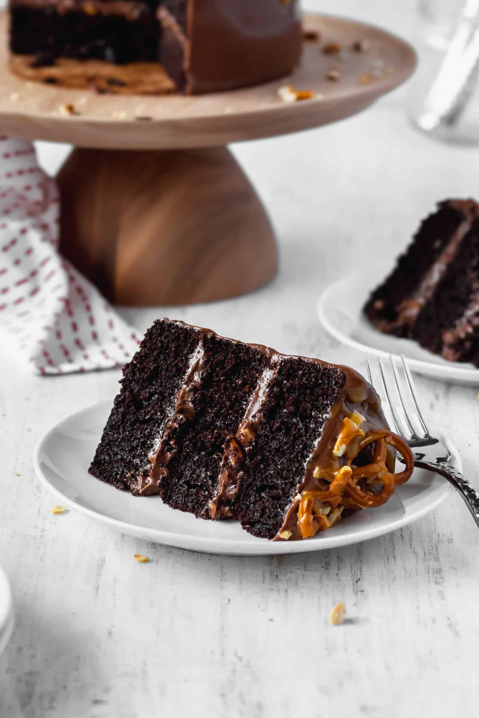 A slice of moist and fluffy chocolate cake with peanuts, pretzels, and chocolate buttercream frosting