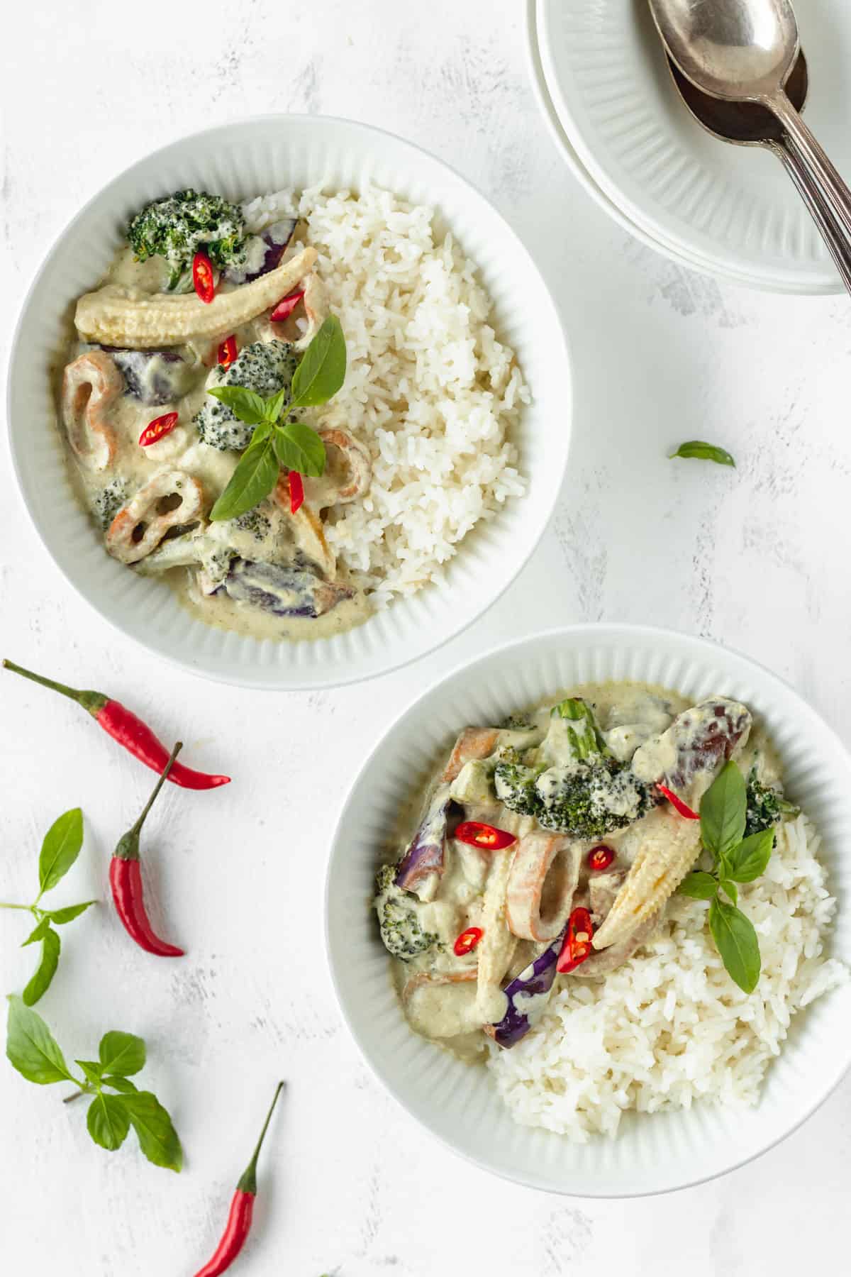 Two bowls of vegan green curry on a white surface.