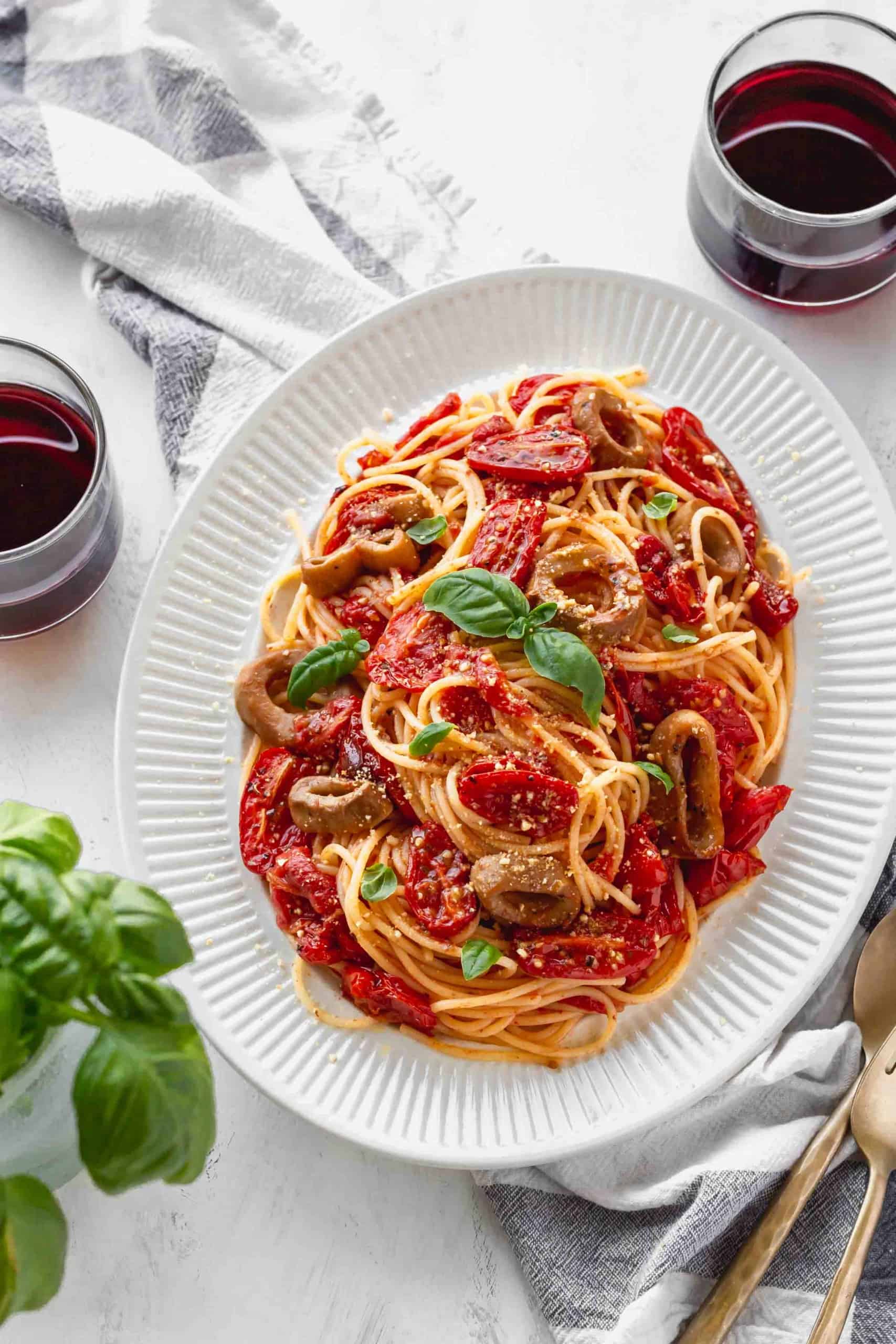 Plate of spaghetti with roasted tomatoes and vegan calamari with two glasses of red wine