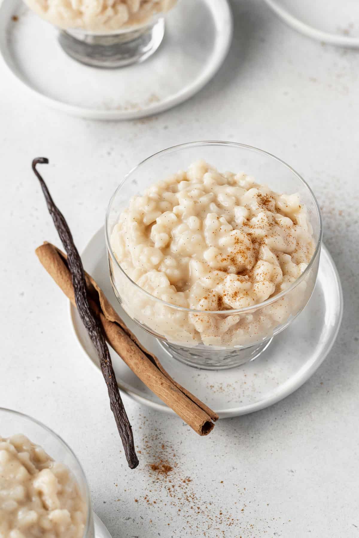 Vegan rice pudding in a dessert glass with a cinnamon stick and vanilla bean placed next to it.