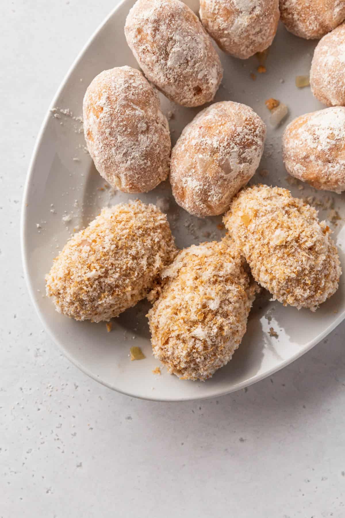 Assembled vegan potato croquettes on a plate showing the various stages of the standard breading procedure.