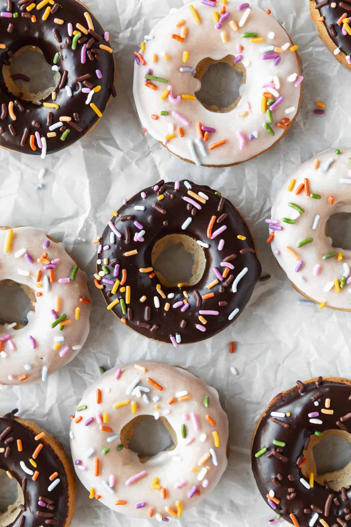 Close up shot of vanilla and chocolate glazed vegan baked donuts on a crumpled piece of parchment.