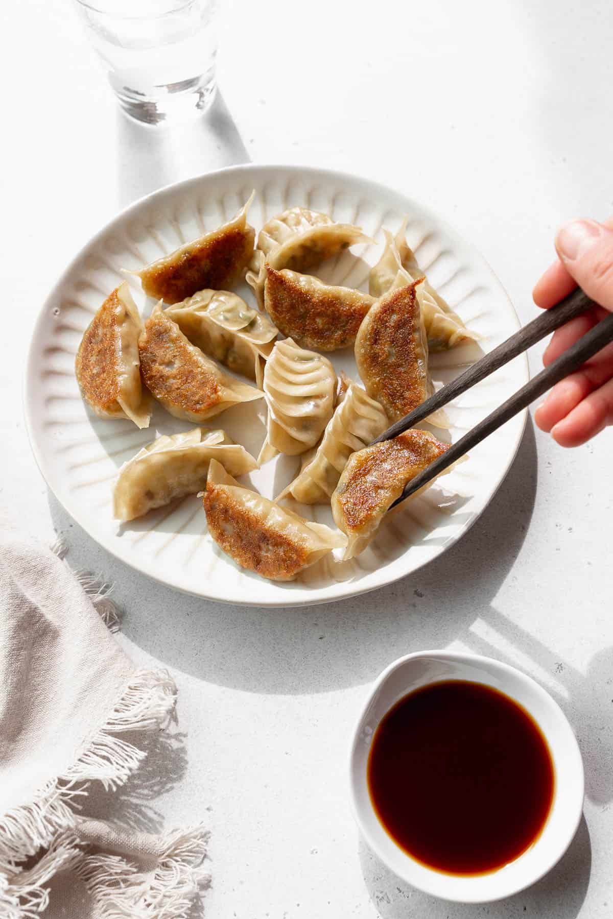 A hand holding chopsticks reaching to pick up a vegan gyoza off a plate. 