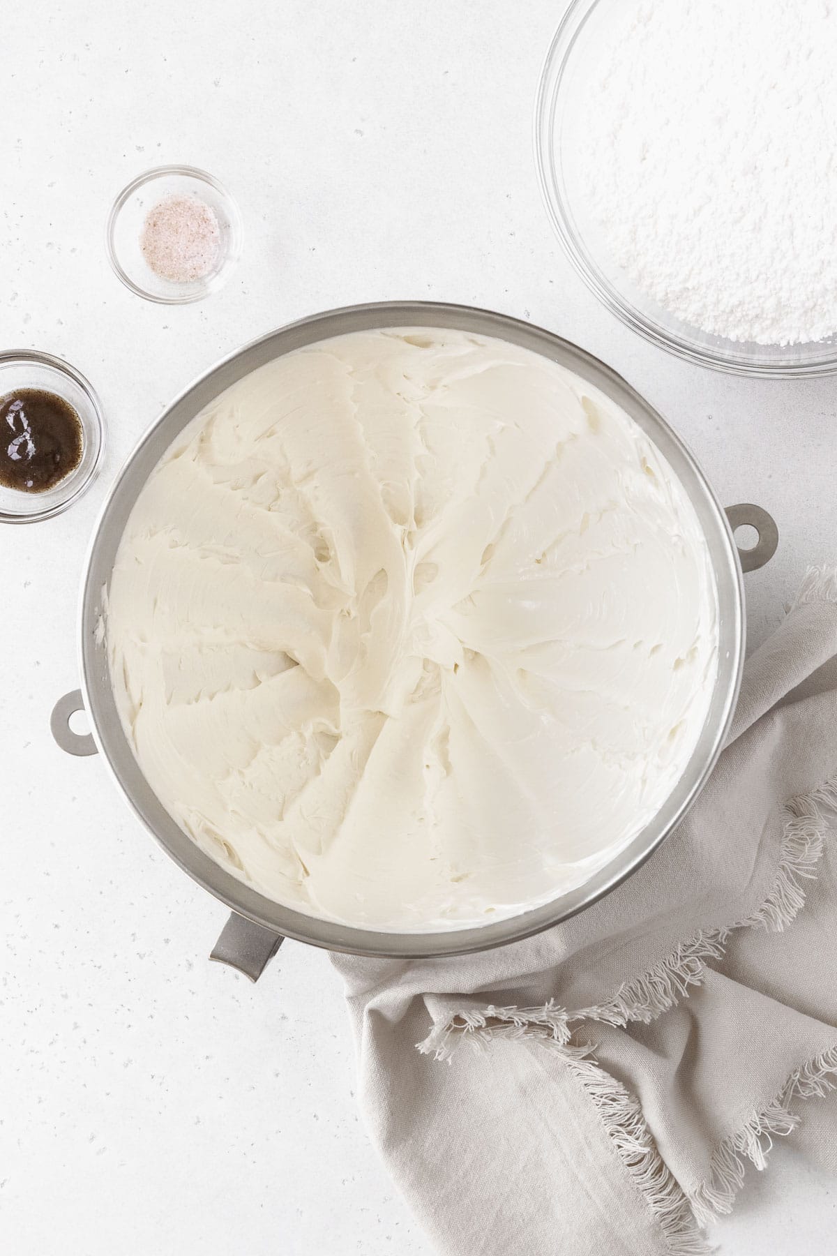 A silver mixing bowl of whipped butter next to a bowl of powdered sugar and vanilla.