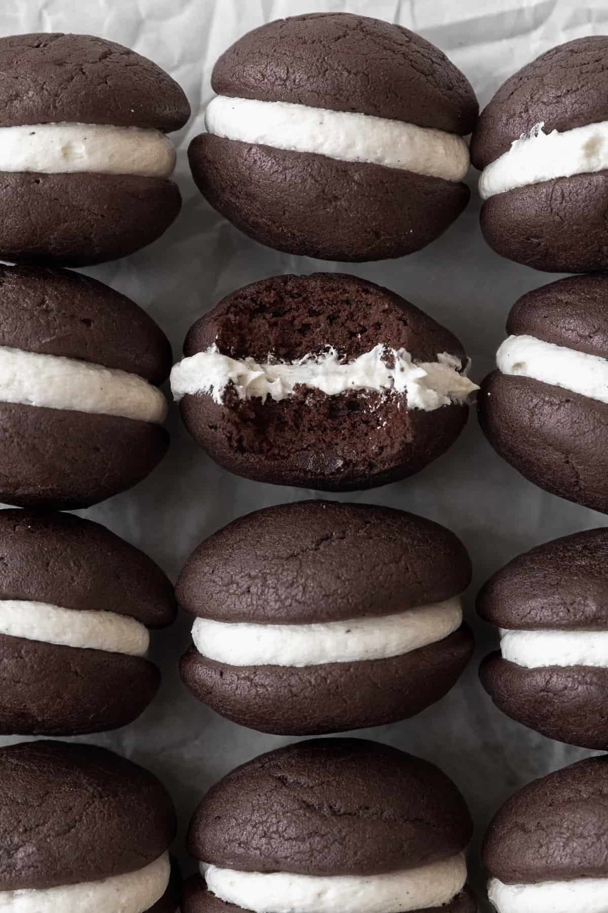 Gluten-free whoopie pies on a white sheet of parchment paper. One of the cookies has a bite taken out of it.
