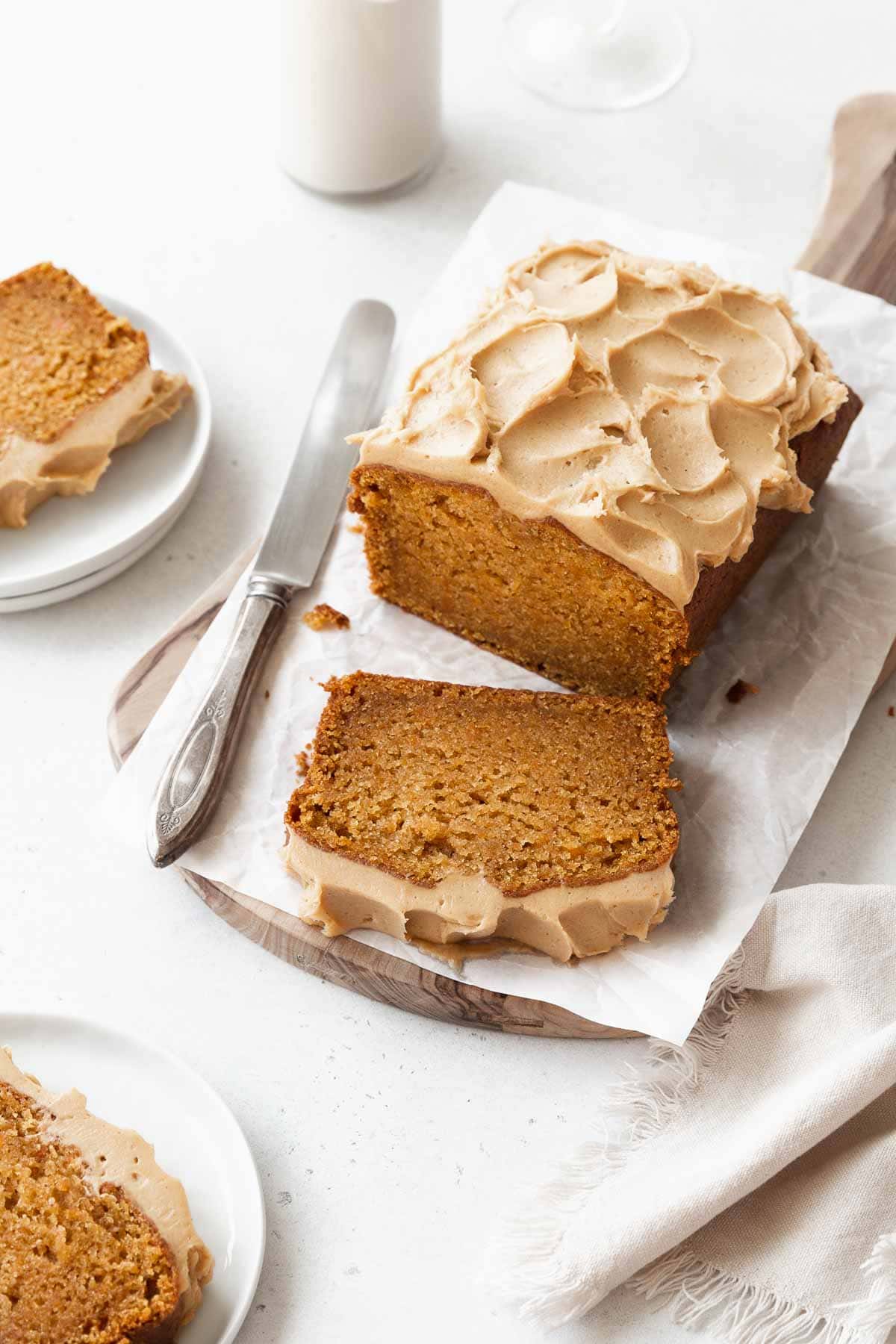 A sliced loaf of gluten-free sweet potato cake with maple frosting with a silver knife next to it.