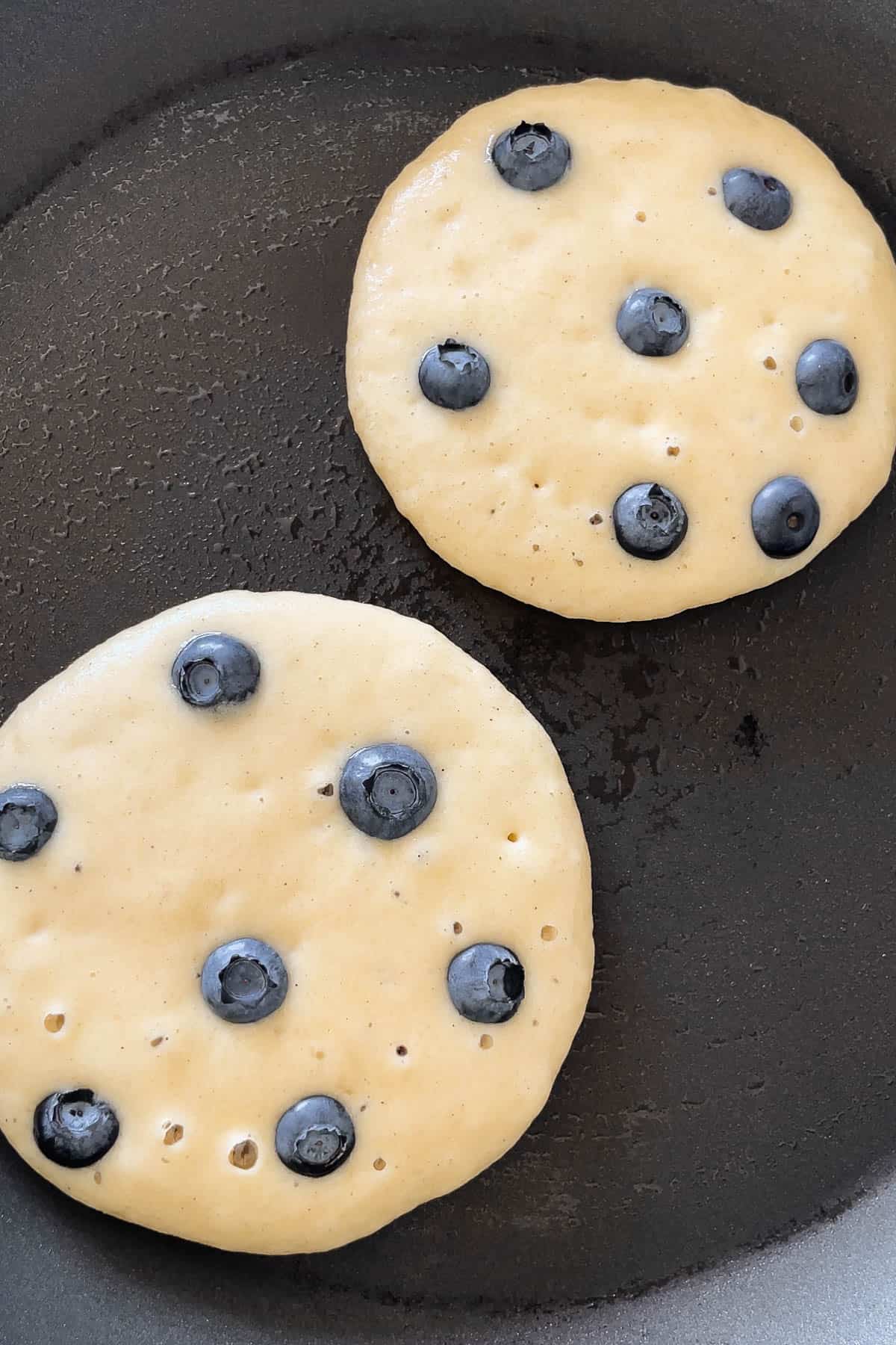 Process shot of 6-8 fresh blueberries added to each pancake on the griddle.
