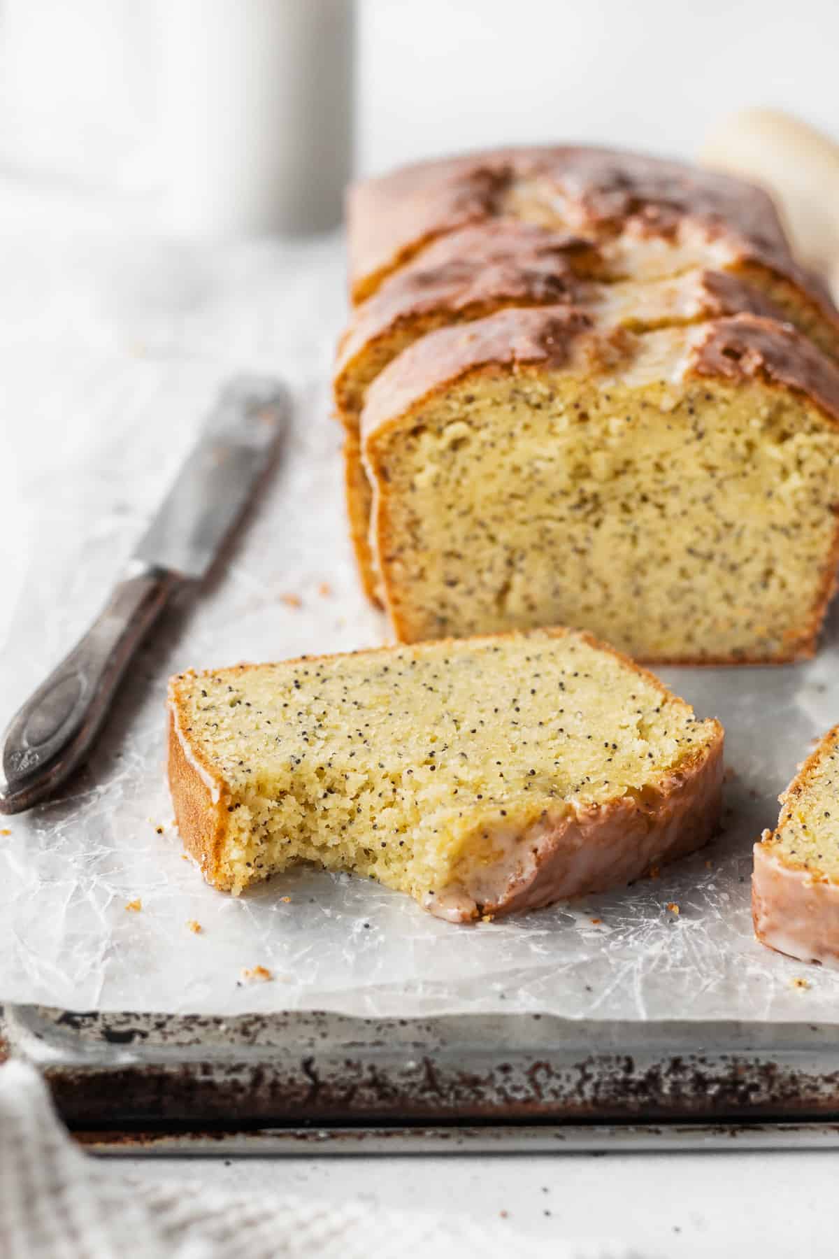 A bitten slice of gluten free lemon bread with the loaf in the background.