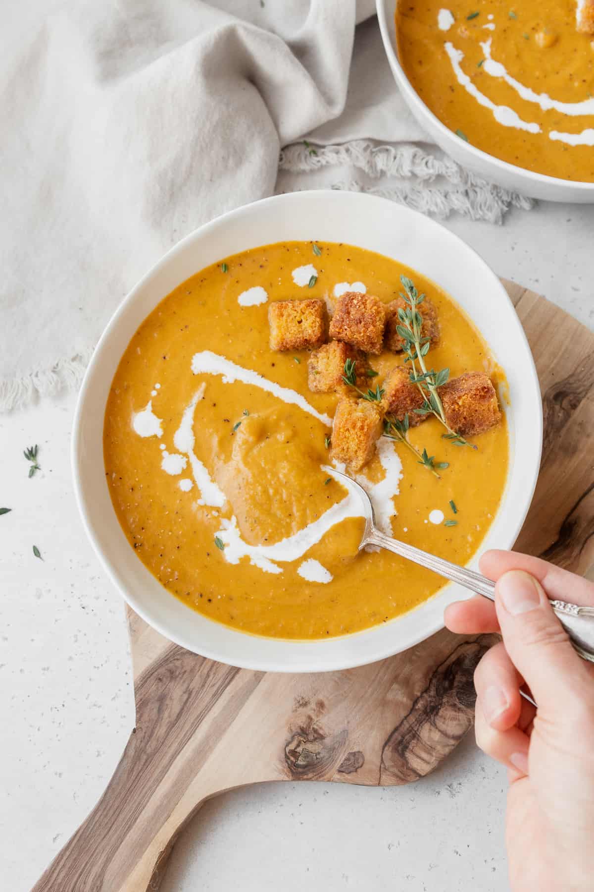 Hand taking a spoonful of vegan pumpkin bisque from the garnished bowl of soup.