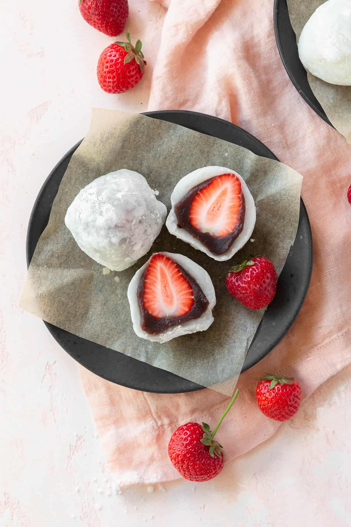 A black plate with a sliced ichigo daifuku next to a whole one. 