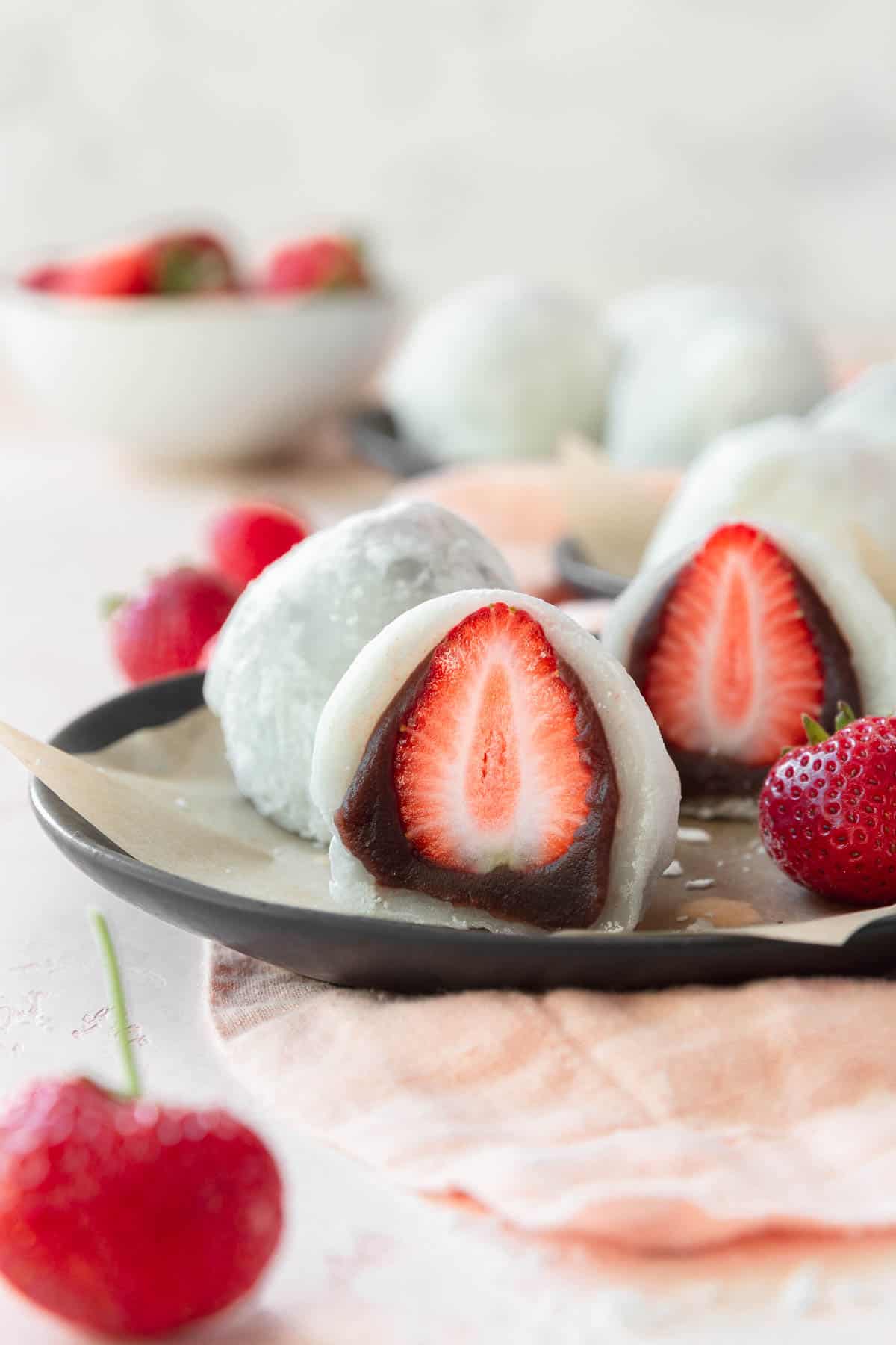 Ichigo daifuku sliced in half placed on a black plate lined with a piece of parchment paper.