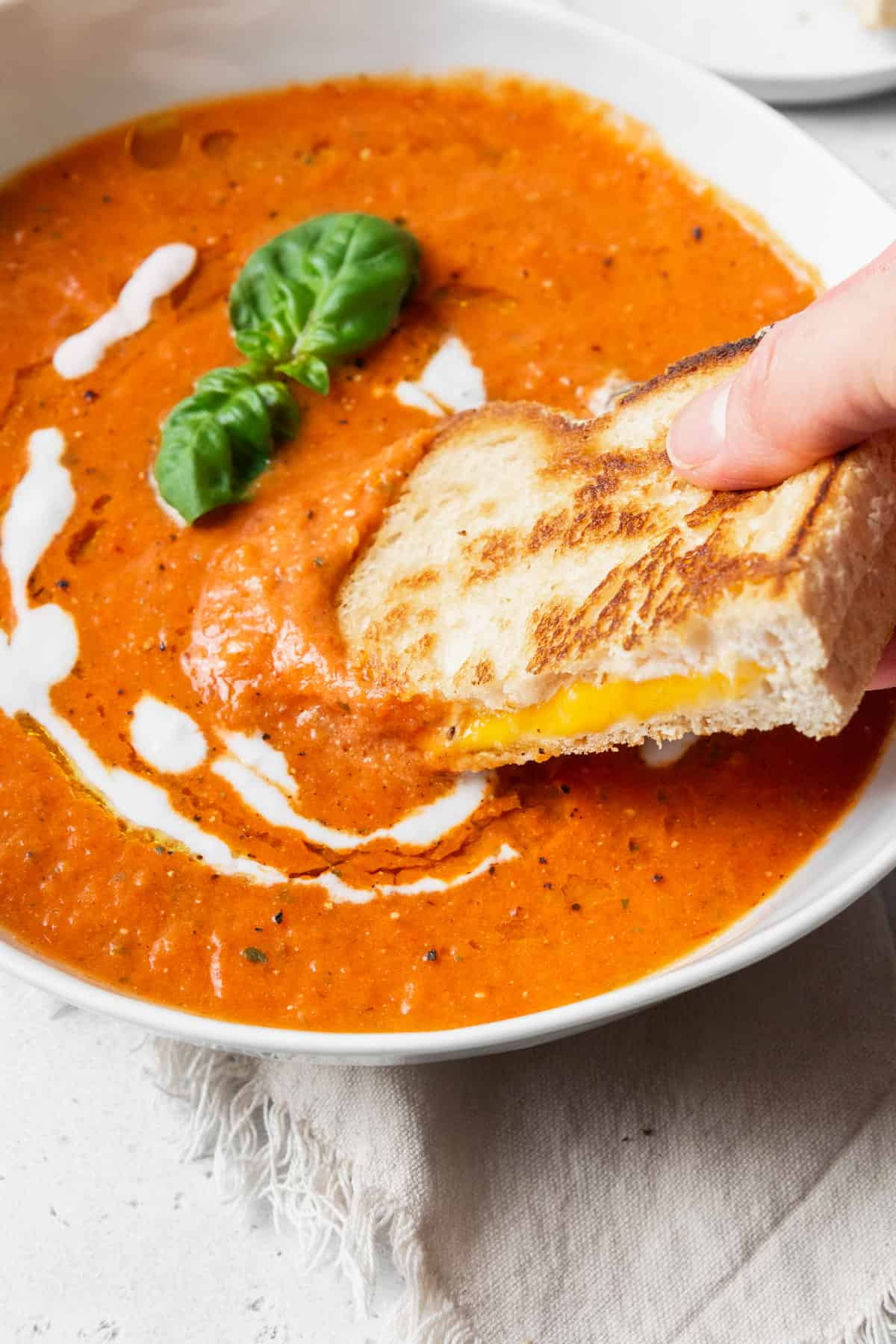 A grilled cheese sandwich being dipped into a bowl of tomato basil soup.