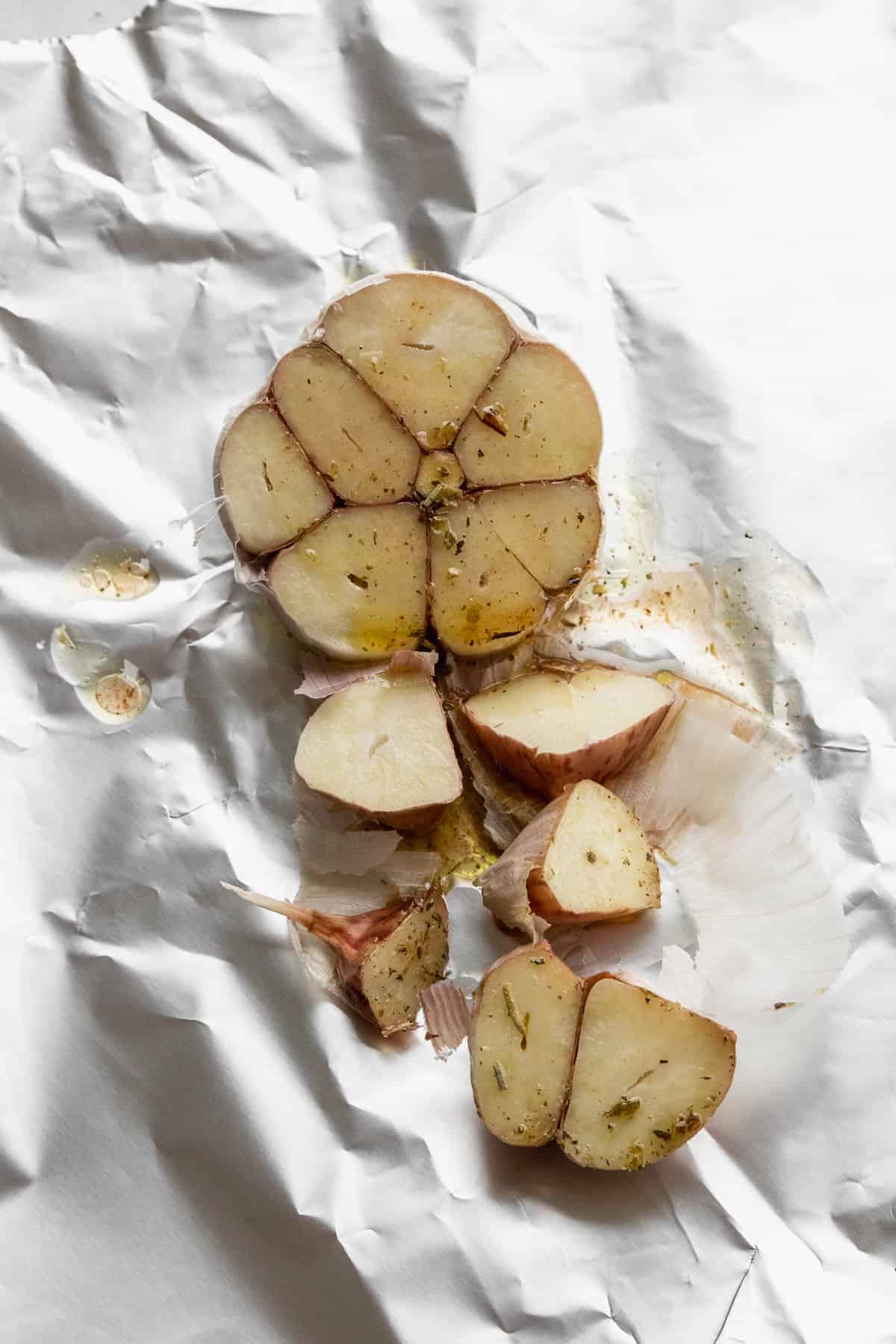 A bulb of garlic sliced in half on aluminum foil and drizzled with olive oil. 